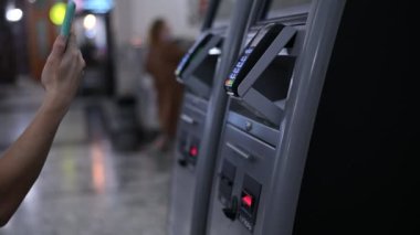 Bir kadın tren bileti almak için self-servis kasasında cep telefonuyla ödeme yapar.