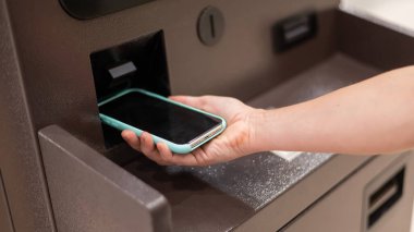 ATM 'de akıllı telefon kullanan bir kadın. NFC çevrimiçi bankacılık kavramı