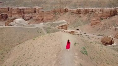 İHA 'nın üst görüntüsü. Kırmızı elbiseli beyaz kadın Kazakistan 'daki Charyn Kanyonu boyunca yürüyor.