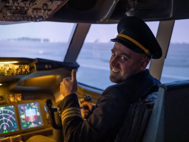 Uçuş simülatörü kullanırken gülümseyen beyaz sakallı bir adam. Pilot kokpitte baş parmak gösteriyor.