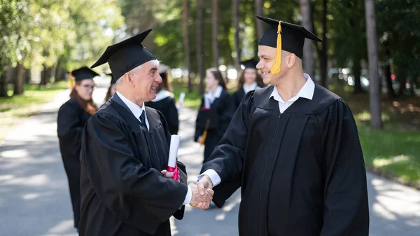 Group Graduates Robes Outdoors Elderly Man Young Guy Congratulate Each — Φωτογραφία Αρχείου