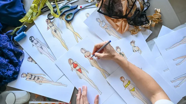 Faceless woman draws sketches of swimwear with a pencil. Top view of the hands of a fashion designer
