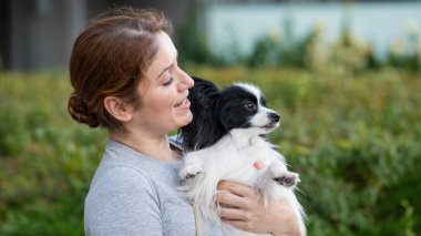 Beyaz, kızıl saçlı bir kadın, pappilion köpeğini açık havada tutuyor. Siyah ve beyaz kıtasal spanyel.
