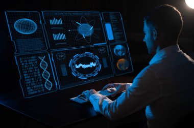 Caucasian man sitting in the dark in front of a virtual menu and typing on a keyboard