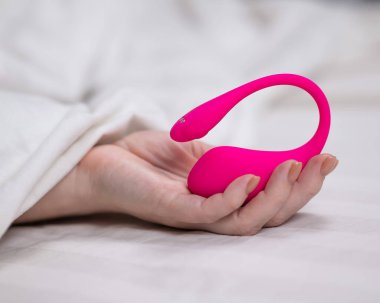 Yatakta uzanırken kavisli pembe vibratör tutan kadın.