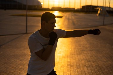 A man trains in boxing at the stadium at sunset. Athlete silhouette