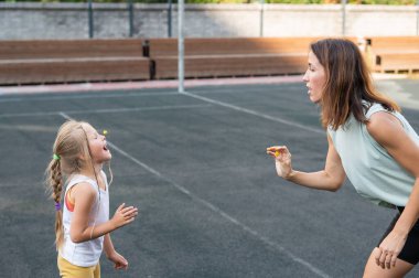 Anne ve kızı açık hava spor sahasında eğleniyor. Beyaz bir kadın şeker atar ve bir kız ağzıyla yakalar.