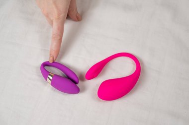 Kadın yatakta yatarken pembe ve mor vibratörler arasında seçim yapıyor.