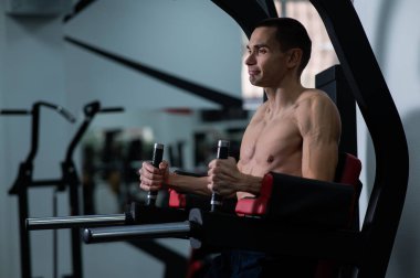 Shirtless man doing triceps dips from parallel bars in gym
