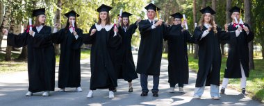 Group of graduates in robes dancing outdoors. Elderly student