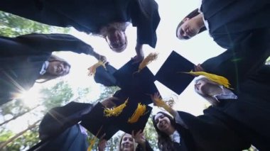 Mezuniyet elbisesi giyen sınıf arkadaşları şapkalarını dışarı atıyorlar. Alt görünüm