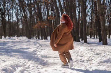 Portrait of an excited red-haired curly fat woman in the park in winter