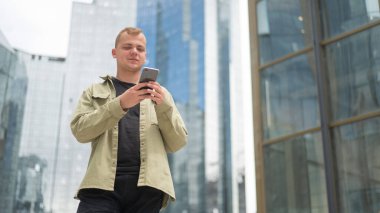 Genç beyaz adam şehir merkezinde akıllı telefon kullanıyor.