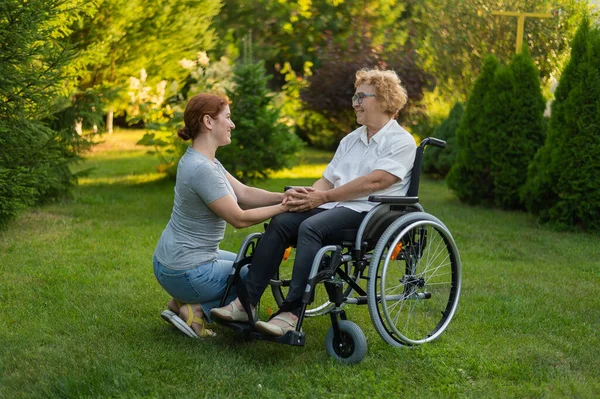 一位高加索妇女牵着一位坐在轮椅上的年长母亲的手 出去走走 — 图库照片