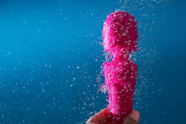 一个女人用蓝色的衬底在流动的水中洗粉红的振子 性玩具卫生概念 — 图库照片