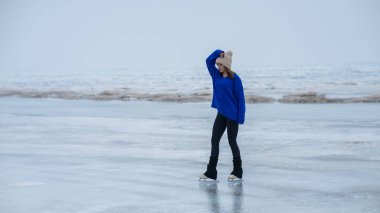 Caucasian woman in a blue sweater skating on a frozen lake