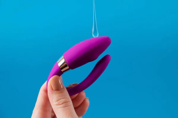 青い背景で潤滑に湾曲したセックスのおもちゃを持っている女性 膣口バイブレータ — ストック写真