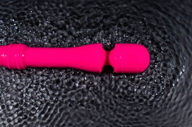 The pink dildo creates a vibration on the surface of the water. Sex toy on a black background