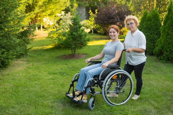 一位老年妇女背着一个坐在轮椅上的成年女儿 出去走走 — 图库照片