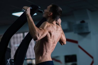 Back view of shirtless man with pull-ups in gym