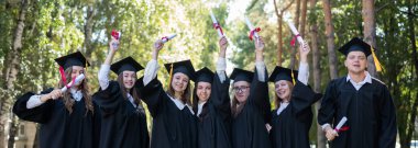 Mezuniyet elbisesi giymiş, açık havada diplomalarını gösteren bir sürü genç öğrenci. Geniş Ekran