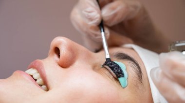 Kirpik kaplama prosedüründeki bir kadının yakın plan portresi. Usta kirpiklere renk katar.