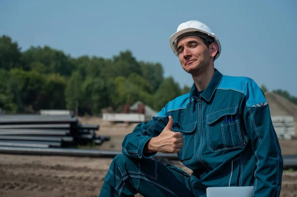 stock image Construction worker holding laptop and showing thumb up while standing at construction site