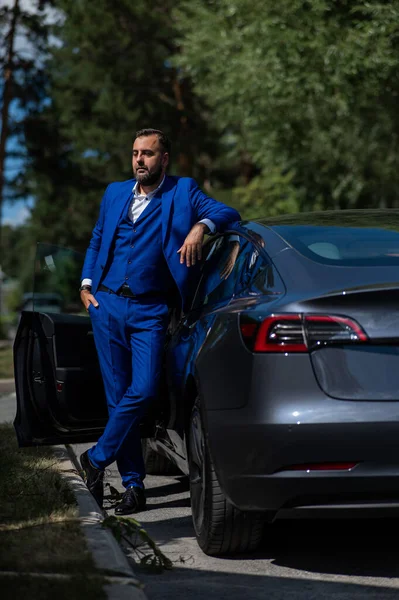 Kaukázusi Szakállas Férfi Kék Öltönyben Kiszáll Egy Fekete Elektromos Autóból — Stock Fotó