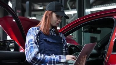 Kadın oto tamircisi dizüstü bilgisayar kullanarak arabada teşhis koyuyor.