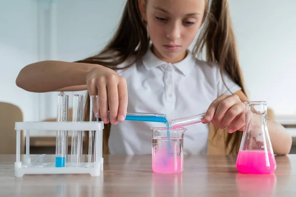 stock image A schoolgirl conducts experiments in a chemistry lesson. Girl pouring colored liquids from a beaker