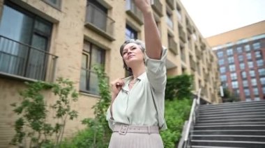 Olgun, beyaz bir kadın caddedeki bir akıllı telefondan selfie çekiyor. Video 360 derece döndürür