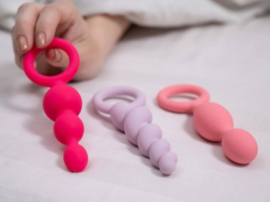 Bir kadın yatakta yatarken bir setten anal boncuk seçer.