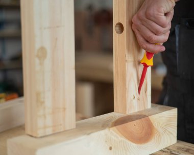 Caucasian man assembles the table with a screwdriver. Close-up of a carpenters hands