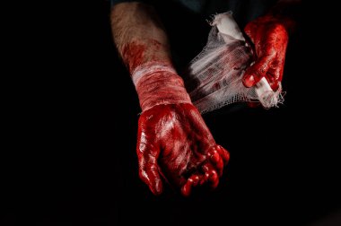 Kanla kaplı bir adam ellerini bandajlıyor.