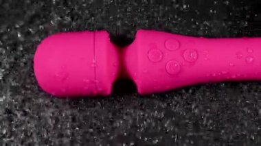 The pink dildo creates a vibration on the surface of the water. Sex toy on a black background