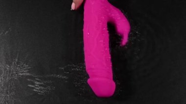 A woman holds a pink dildo in the water. Sex toy on a black background