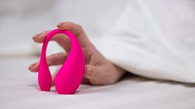 Yatakta uzanırken kavisli pembe vibratör tutan kadın.
