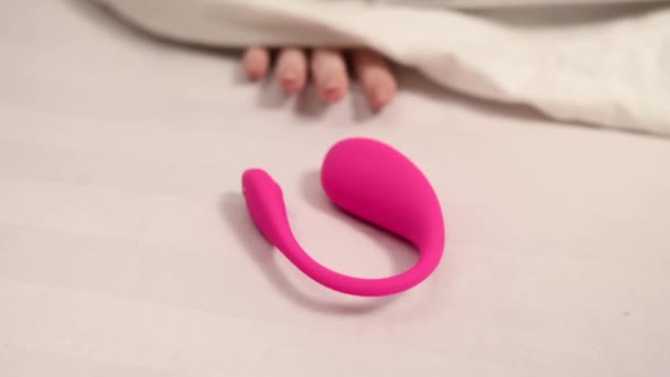 一个女人的手从白色毛毯下伸出来 拿着一个阴道口的性爱玩具 — 图库视频影像