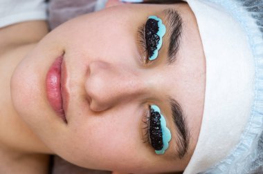 Bir kadının yakın plan portresi, kirpik boyama ve kaplama prosedürü üzerine. Kalıcı makyaj