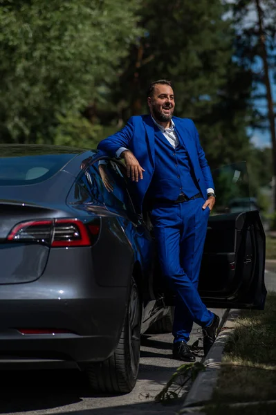 Kaukázusi Szakállas Férfi Kék Öltönyben Kiszáll Egy Fekete Elektromos Autóból — Stock Fotó