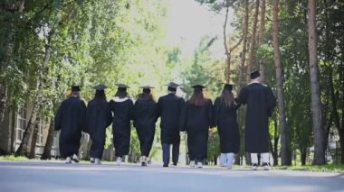 Bir grup mutlu öğrenci akademik şapkalarını havaya fırlatıyorlar. Yavaş çekim