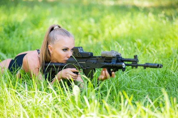 身穿比基尼的白人女人躺在绿草上拿着机枪 — 图库照片