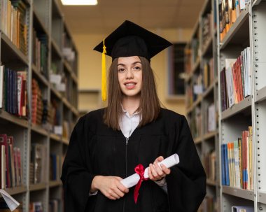 Mezuniyet elbisesi içinde, elinde diploması olan mutlu genç bir kadın.