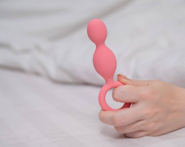 Yatakta uzanmış pembe anal boncuklu bir kadının yakın çekimi.