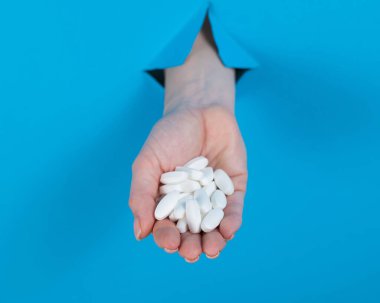 Bir kadın bir avuç dolusu hap tutuyor. Bir kadın elleri karton mavi bir arka planda bir delikten sarkıyor.