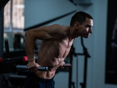 Shirtless man doing triceps dips from parallel bars in gym