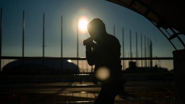 Tişörtlü bir adam gün batımında stadyumda boks antrenmanı yapıyor. Atlet silueti