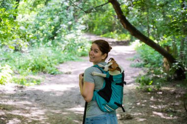 Beyaz bir kadın özel bir sırt çantasıyla köpek Jack Russell Terrier ile dışarı çıkıyor.