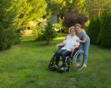 Beyaz bir kadın tekerlekli sandalyede oturan yaşlı bir anneye sarılıyor. Dışarı çık.