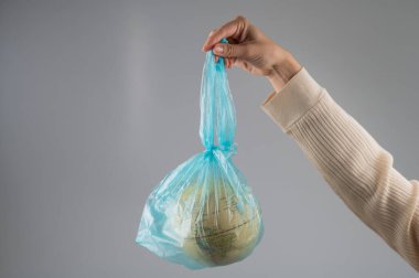 Beyaz arka planda plastik bir torba içinde bir kadın elinde bir küre tutuyor.